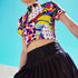 A colorful 90s-style mesh crop top featuring a maximalist abstract pattern. This see-through shirt has a high mock neck, short sleeves, and a vibrant, retro design with geometric shapes, color blocking, and polka dots in bold shades of pink, yellow, blue, and orange. The Y2K-inspired top is a statement piece of festival clothing, perfect for a rave outfit or alternative, dopamine-dressing-inspired streetwear looks.